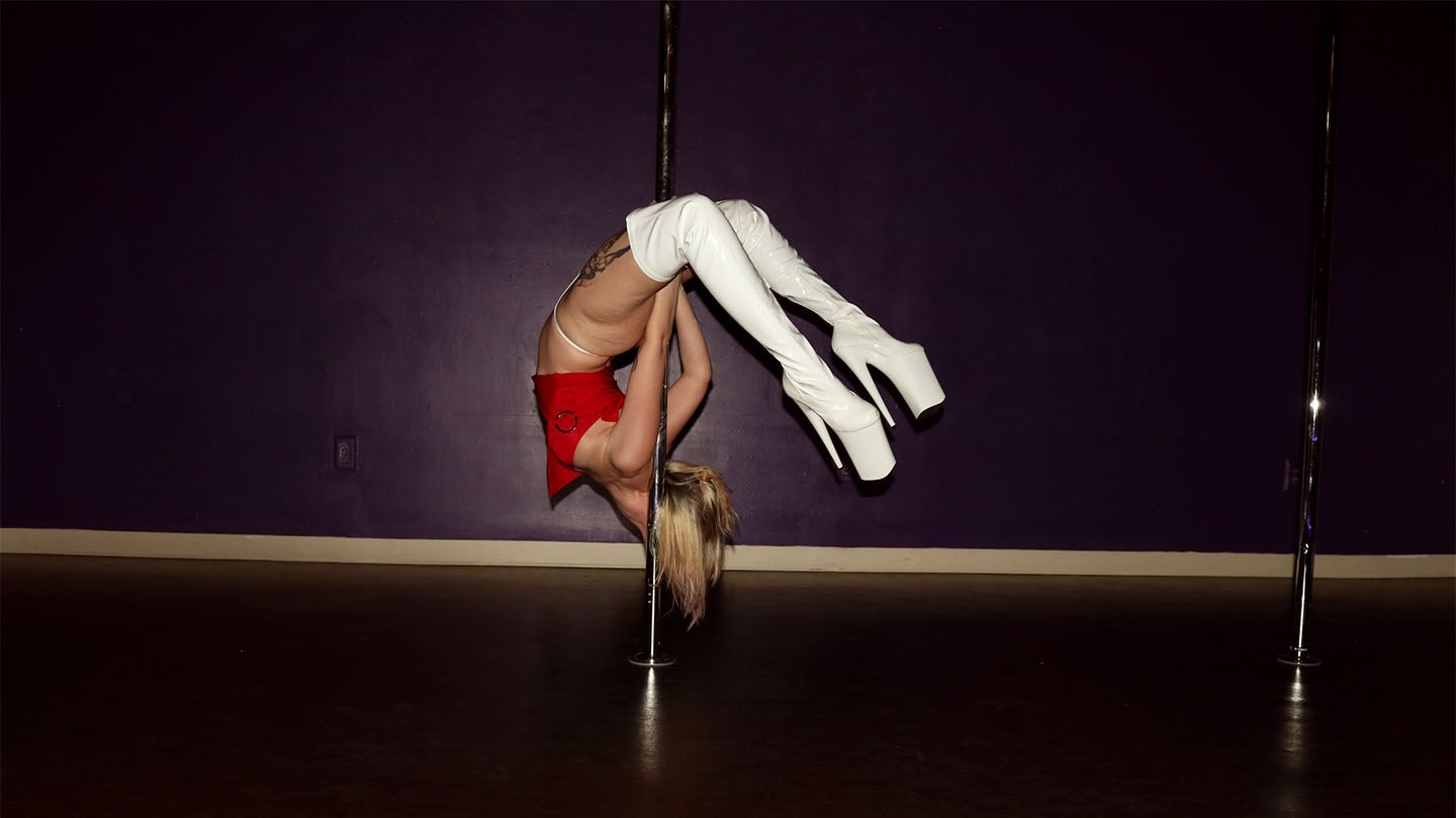 Solo dancer upside down on a pole, wearing a red outfit and white thigh-high boots